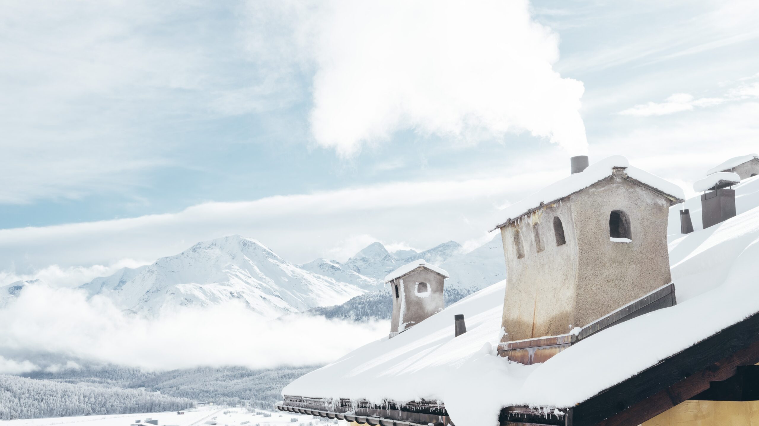 A wide shot of a house near mountains covered in snow